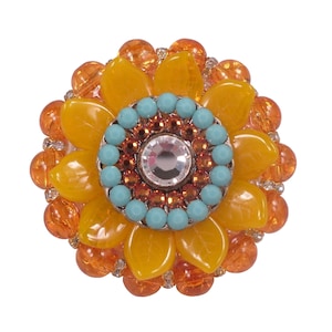 以下が含まれることがあります： オレンジ色のビーズで囲まれたターコイズとクリアクリスタルの中心を持つ、黄色のひまわり型のブローチです。