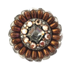 May include: A round, copper-colored beaded brooch with a central square crystal surrounded by smaller crystals in shades of pink and clear.