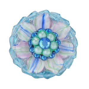 Op de afbeelding: Een blauw en wit bloemvormig decoratief stuk met een centrum van blauwe en groene strass.