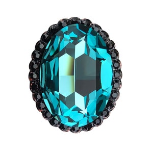 May include: An oval-shaped, faceted teal gemstone with a dark, beaded border. The gem has a multi-faceted surface that reflects light, creating a shimmering effect. The dark border adds contrast to the bright teal color.