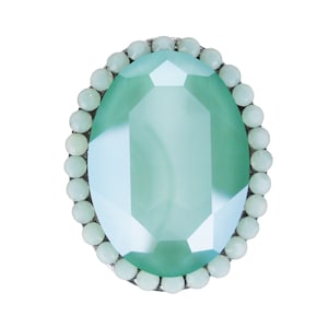 Könnte beinhalten: Ein ovaler Ring in hellgrün mit einem großen facettierten Edelstein, der von einem Rand aus kleineren weißen Perlen umgeben ist.