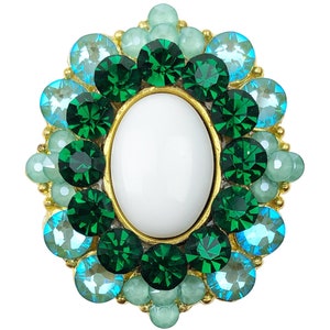 Peut inclure: Une broche dorée avec une pierre ovale blanche au centre entourée de strass verts et bleus.