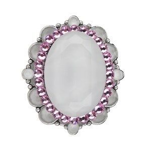 Peut inclure: Une broche ovale en argent avec un centre en pierre blanche entouré d'un anneau de strass roses.