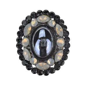 May include: A black oval ring with a large, dark gray gemstone surrounded by smaller, clear and gold-toned gemstones.