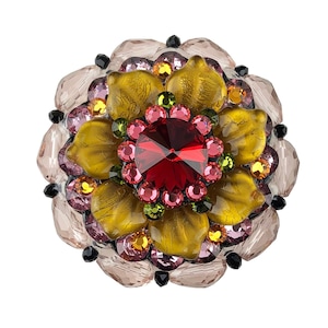 以下が含まれることがあります： 中央に赤い宝石、その周りをピンク、イエロー、グリーンの小さな宝石で囲んだ、大きな多色のブローチ。ブローチは、黄色の中心とピンクの花びらを持つ花の形をしています。
