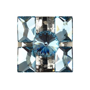 May include: A square-shaped crystal knob with a large, faceted, light blue crystal in the center. The knob is surrounded by four smaller, light blue, faceted crystals.
