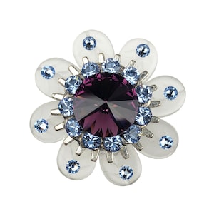 以下が含まれることがあります： 中央に大きな紫色のラインストーン、周囲に小さな青いラインストーンが散りばめられた、銀色の花の形をしたブローチです。