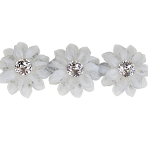 Puede incluir: Tres pinzas para el pelo de color blanco con forma de flor y centros de cristal transparente.