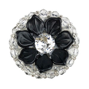 以下が含まれることがあります： 中央に大きな透明なラインストーンが置かれ、小さなラインストーンで囲まれた黒い花のブローチです。