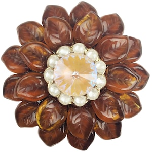 Könnte beinhalten: Eine braune Brosche aus Kunstharz in Blütenform mit einem klaren Strassstein in der Mitte, umgeben von Perlenimitationen.