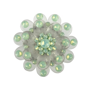 May include: A clear plastic flower brooch with a center cluster of light green iridescent rhinestones.