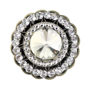 May include: A round, antique gold-toned brooch with a large, clear crystal in the centre. The crystal is surrounded by a ring of smaller crystals and a decorative border.