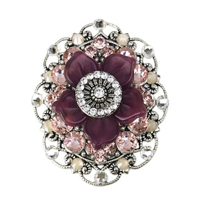 以下が含まれることがあります： 紫色の花のデザインが施された銀色のブローチ。花の中心にはクリアなラインストーンが、周りをより小さなピンクのラインストーンが囲んでいます。