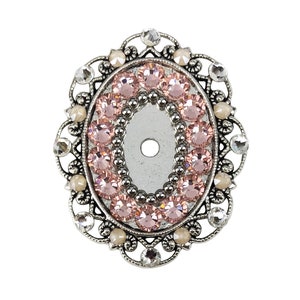 以下が含まれることがあります： 繊細なフィリグリーのデザインが施された、楕円形の銀色の金属製の装飾品。装飾品は、ピンクのラインストーンの円と、より小さな透明なラインストーンの円が飾られています。