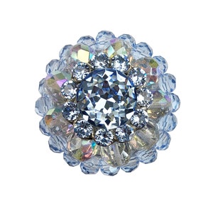 May include: A large blue rhinestone brooch with a central, faceted, blue crystal surrounded by smaller rhinestones.