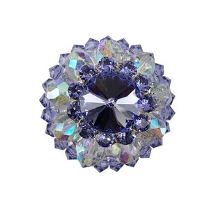 Peut inclure: Une broche ronde et irisée de couleur violette avec un grand cristal facetté de couleur violet foncé au centre.