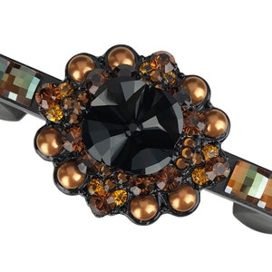 Può includere: Un fermaglio per capelli in metallo nero con un grande strass nero circondato da strass più piccoli e perline dorate.