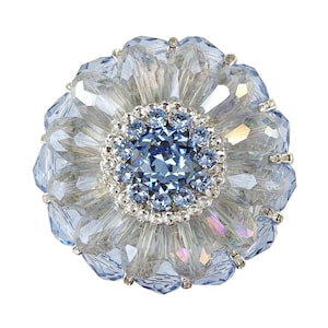 May include: A large, blue crystal flower brooch with a central blue stone surrounded by smaller crystals.