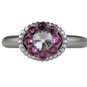 Könnte beinhalten: Ein silberner Ring mit einem großen, klaren Kristall, der von einem Kreis aus kleineren rosa Kristallen umgeben ist.