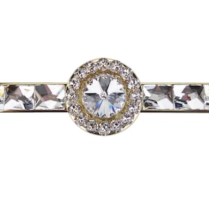 May include: A gold-toned drawer pull with a large, clear crystal in the center surrounded by a halo of smaller crystals.