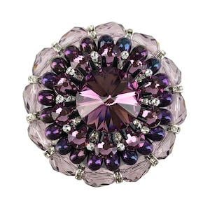 以下が含まれることがあります： 中央にファセットカットされたアメジスト色のクリスタルが施され、その周りをクリアとパープルの小さなクリスタルが囲む、大きく丸いパープルのブローチです。