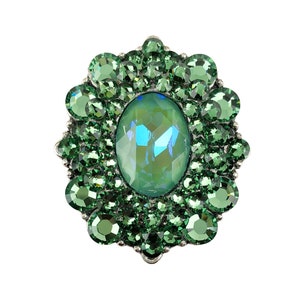 May include: A green jeweled ring with a large oval-shaped center stone surrounded by smaller stones.