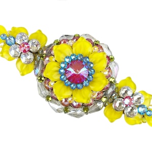 Puede incluir: Un broche de flor amarilla con adornos de cristal y pedrería. El broche está hecho de metal y tiene un diseño floral.