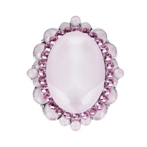 Peut inclure: Une broche ovale en argent avec une grande pierre ovale rose pâle entourée d'une bordure de strass roses.