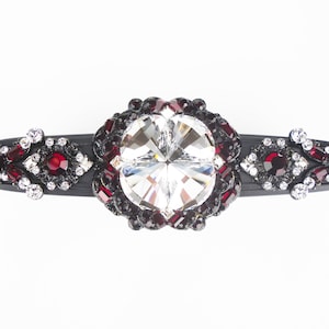 May include: A black hair clip with a large clear crystal surrounded by smaller red and black crystals.