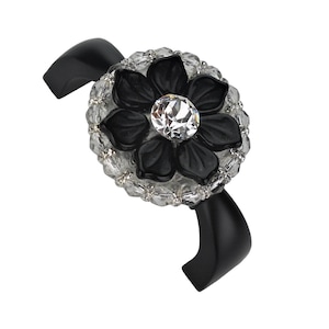 Könnte beinhalten: Ein schwarzes Armband mit einem zentralen Blumendesign. Die Blume hat schwarze Blütenblätter, die einen großen, klaren, facettierten Edelstein umgeben. Die Blume ist von klaren, facettierten Perlen umgeben. Das Armband ist schwarz und gebogen.