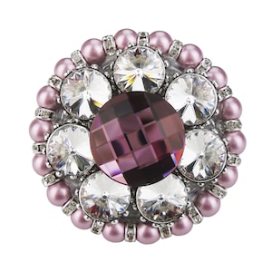 May include: A round brooch featuring a large, faceted, purple gemstone surrounded by smaller, clear gemstones and a ring of pink pearls.