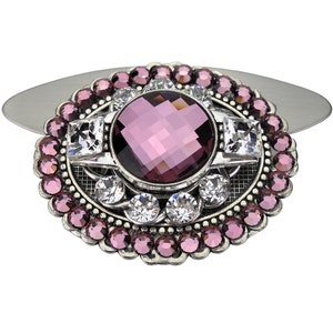 May include: A silver oval brooch with a large, faceted, purple gemstone surrounded by smaller clear rhinestones. The brooch is decorated with a silver filigree design.
