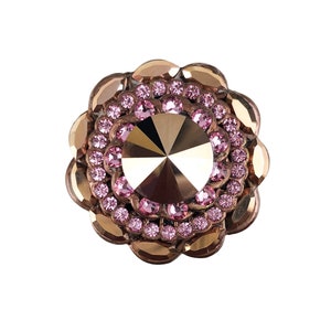 以下が含まれることがあります： 中央に大きなファセットカットの透明なクリスタルが置かれ、その周りを2列の小さなピンクのクリスタルが囲む、金色の花の形をした装飾品