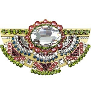 Può includere: Un fermaglio dorato con un grande cristallo trasparente al centro. Il fermaglio è decorato con strass rossi, verdi e blu in un motivo geometrico.