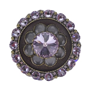 Könnte beinhalten: Ein runder, mit violetten und goldenen Schmucksteinen besetzter Knopf mit einem großen, facettierten, violetten Kristall in der Mitte.