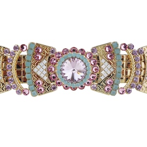 Op de afbeelding: Een gouden haarspeld met een geometrisch ontwerp en roze en blauwe strass steentjes. Het midden van de speld heeft een grote, heldere strass steen.