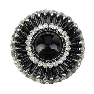 Könnte beinhalten: Eine schwarze und silberne Brosche mit einem großen schwarzen Edelstein, der von kleineren Strasssteinen umgeben ist.