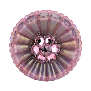May include: A pink glass button with a flower design made of smaller pink rhinestones. The button has a textured, iridescent surface.