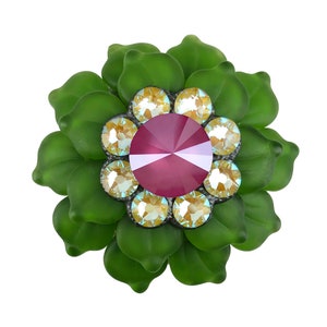 May include: A green glass flower with a pink rhinestone center and clear rhinestones around it.