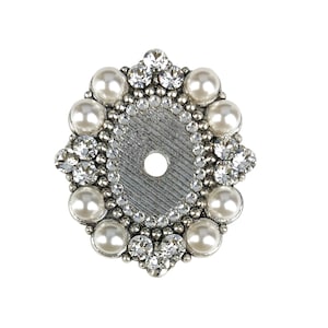 以下が含まれることがあります： 円形のデザインの銀色の装飾品。この作品は、模造真珠とラインストーンのリングで飾られています。