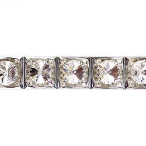 May include: A silver bracelet featuring five large, square-cut, clear crystals. Each crystal is set in a silver frame, creating a sparkling, elegant design. The bracelet is displayed against a white background, highlighting its brilliance.