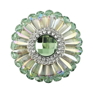 May include: A green and iridescent flower-shaped brooch with a large green rhinestone in the centre surrounded by smaller clear rhinestones.