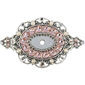 May include: A silver-toned oval-shaped brooch with a delicate filigree design. The centre of the brooch is adorned with a cluster of pink rhinestones.