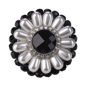 May include: A black and white flower-shaped brooch with a large black gemstone in the centre surrounded by smaller white pearls and black beads.