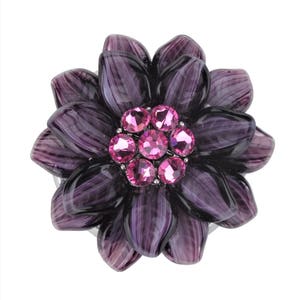 以下が含まれることがあります： ピンクのラインストーンが中心に付いた紫色の花のブローチ