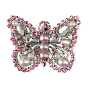 Puede incluir: Un broche de mariposa de plata con pedrería rosa y transparente y detalles de perlas.