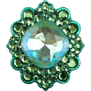 Puede incluir: Un gran cristal azul claro facetado rodeado por un anillo de cristales más pequeños de color verde oscuro. Los cristales están engastados en un marco de metal con un borde festoneado.