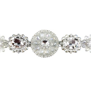 May include: A silver hair clip with five crystal embellishments. The center embellishment is a large round crystal surrounded by smaller crystals. The other four embellishments are smaller, oval-shaped crystals.