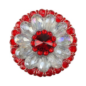 Peut inclure: Une broche en cristal rouge et transparent en forme de fleur. Le centre de la fleur est un grand cristal rouge entouré de petits cristaux rouges. Les pétales de la fleur sont en cristal transparent.