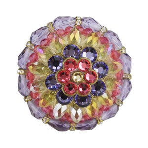Könnte beinhalten: Eine runde, mehrfarbige Brosche mit einem Blumendesign. Die Blume besteht aus roten, rosa und violetten Strasssteinen. Die Brosche ist von einem Ring aus kleineren Strasssteinen umgeben.